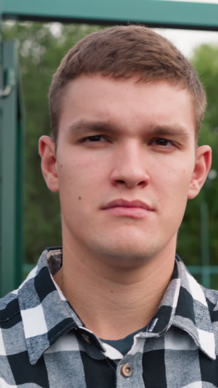 초록색 바와 잔잔한 나무가 배경에 있는 코트에 서있는 젊은 운동 선수의 가까운 얼굴 모습, 결단력과 준비를 구현합니다.