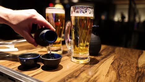 hand pouring sake into small cups by beer glasses