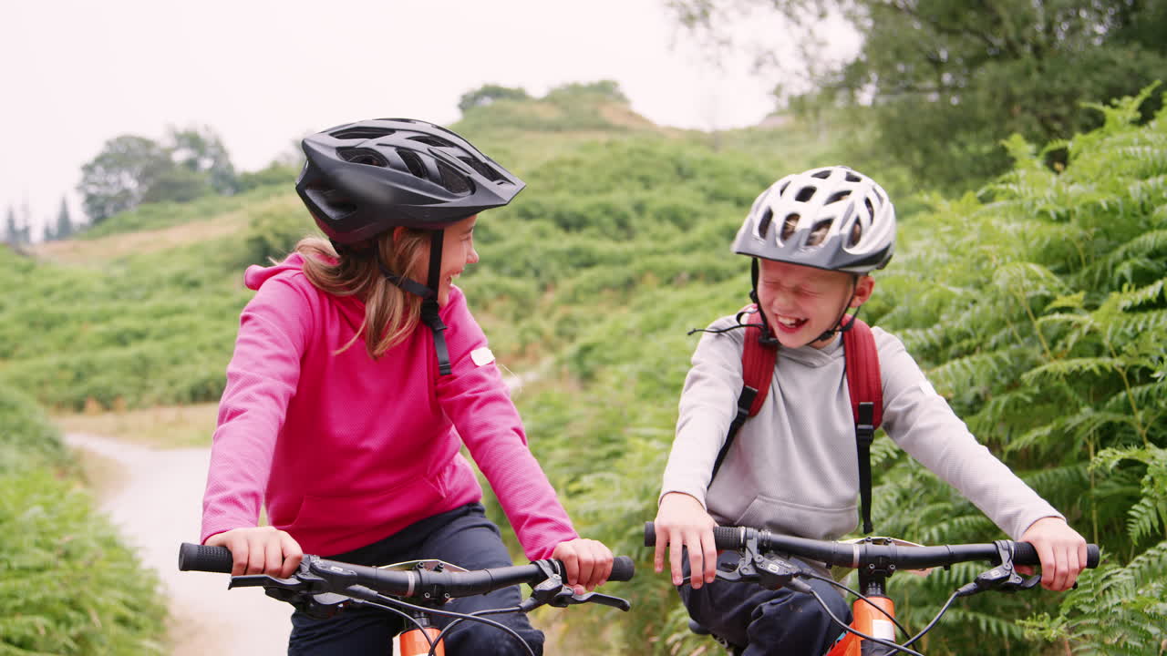 영국 의 레이크 디스트릭트 에 있는 시골 길 에 산악 자전거 를 타고 앉아 있는 두 자녀