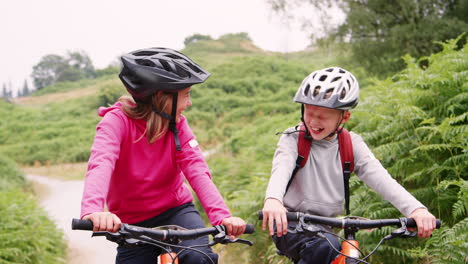 Two-children-sitting-on-their-mountain-bikes-on-a-country-path-laughing,-Lake-District,-UK