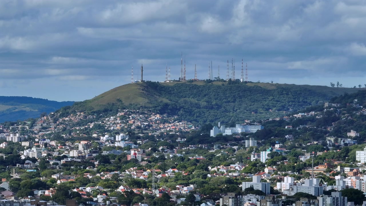 Staattinen ilmakuva metsäisestä kukkulasta, jossa on viestintäantenneja, ja josta avautuu näkymä tiheään kaupunkimaiseen asuinalueeseen Porto Alegressa, Brasiliassa.