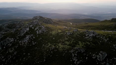 Dunkles,-Launisches-Licht-überquert-Freiliegende-Felsen,-Die-über-Grüne-Hügel-Mit-Kurvenreicher-Straße-Ragen,-Sierra-De-San-Mamede,-Ourense,-Spanien