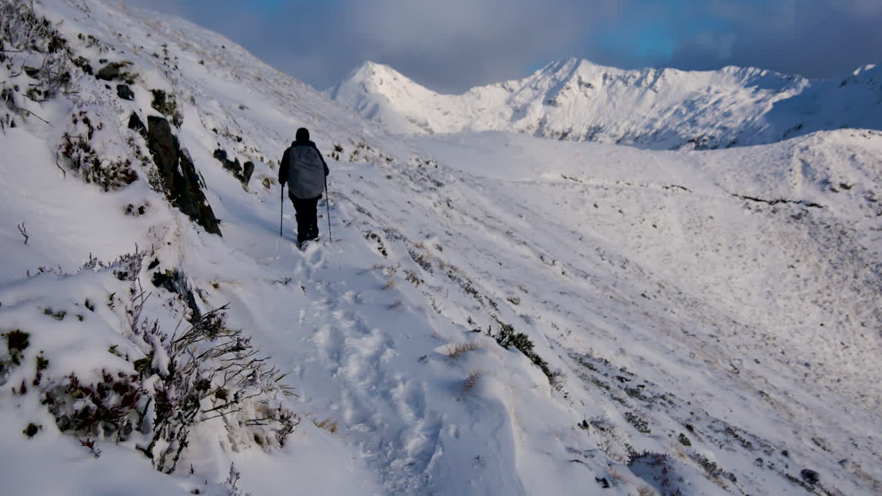 케플러 트랙에서 눈 덮인 절벽의 위험한 가장자리를 따라 걷는 등산용 기둥과 배낭을 든 산악인