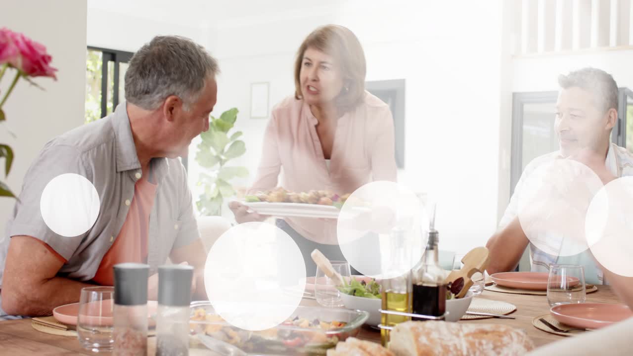 Adults sitting at table, woman entering carrying platter and serving, overlays showing food sharing