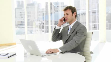 Charming-businessman-on-phone-working-at-a-laptop