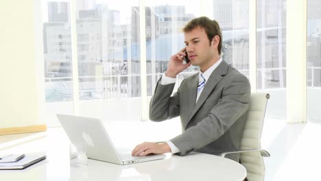 charming businessman on phone working at a laptop