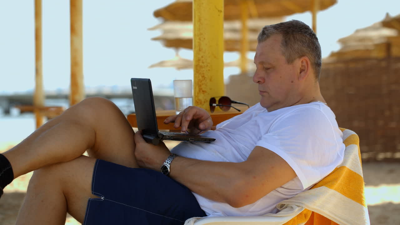 hombre relajándose con una computadora portátil en un resort de playa