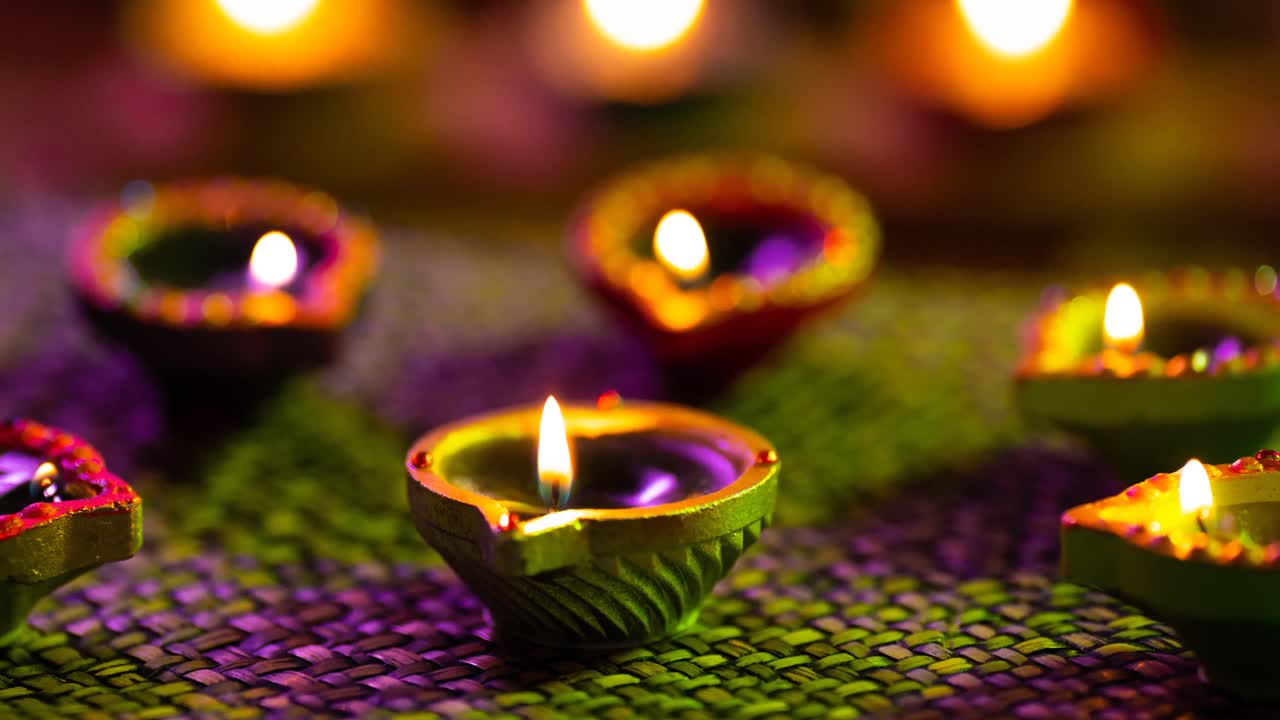 Video of glowing lit diwali candles on woven purple to green surface