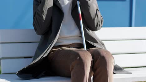 visually impaired man talking on the phone, sitting on the bench in the city.