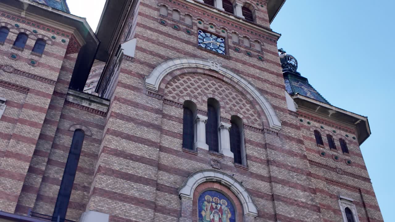 Smooth tilt-up view of Timisoara’s Metropolitan Cathedral, highlighting the detailed brickwork and spires of this historic landmark