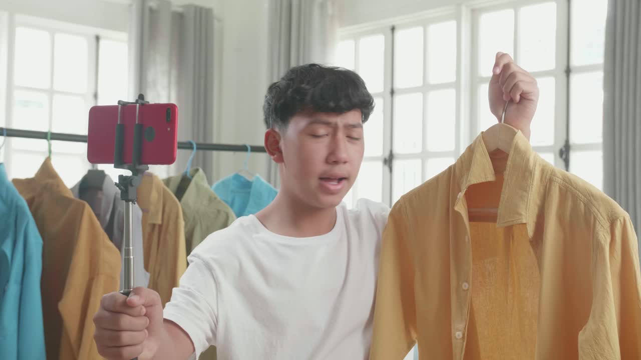 Asian Man Online Seller Recommending A Shirt And Recording Video By Mobile Phone While Selling Clothes At Home