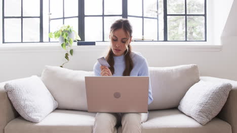 at home, woman shopping online with laptop and credit card, looking focused