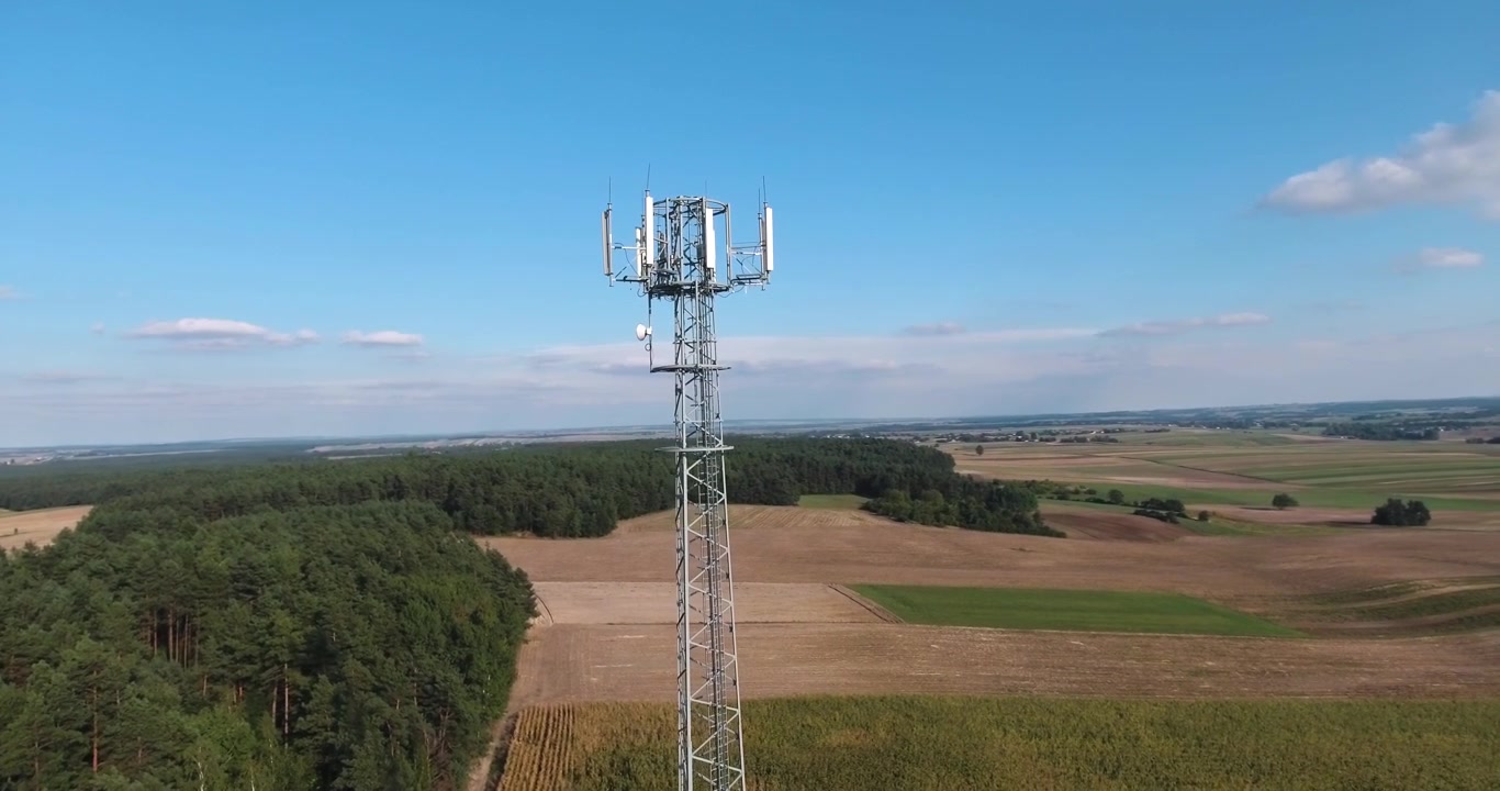 Una torre de transmisión de hierro rodeada de campos en un día soleado de verano con cielos azules y nubes, toma aérea en resolución 4K