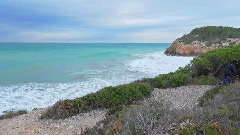 a man on a bicycle is riding along a stony trail that winds its way along untamed coastline of ocean