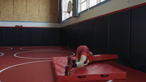 teenage wrestler wearing a red singlet practicing throws on a dummy