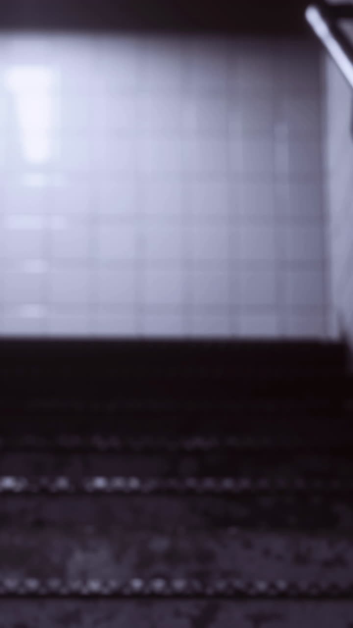 Descent into dimly lit stairway with textured tiles and handrail