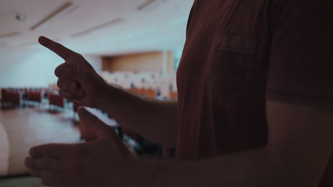 A student uses expressive hand gestures while speaking or explaining something in an empty lecture hall, suggesting preparation, argument, or debate