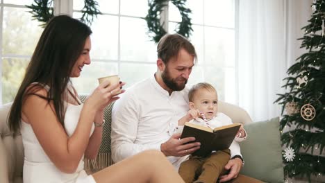 Der-Junge-Vater-Und-Sein-Sohn-Lesen-Ein-Buch,-Während-Die-Mutter-Tee-Trinkt-Und-Ihnen-Zuhört.-Familie-Liest-Weihnachtsgeschichte,-Während