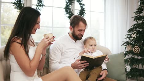 young father and his son reading book, while mother is drinking tea, listening to them. family reading christmas story while