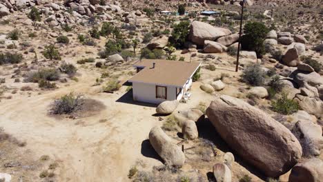 Pequeña-Casa-Solitaria-Junto-A-Una-Enorme-Roca-De-Piedra-En-Un-Desierto-Mortal,-Vista-Aérea