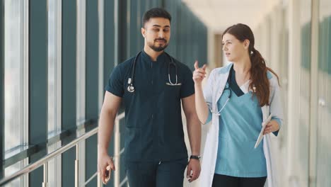 a doctor and a nurse are talking while walking along a hospital corridor with a tablet