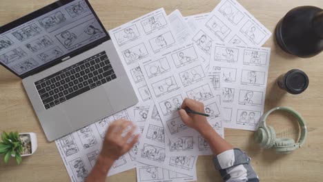 close up top view of asian male artist looking at sketching concept on a laptop and drawing storyboard on table with headphones in the studio