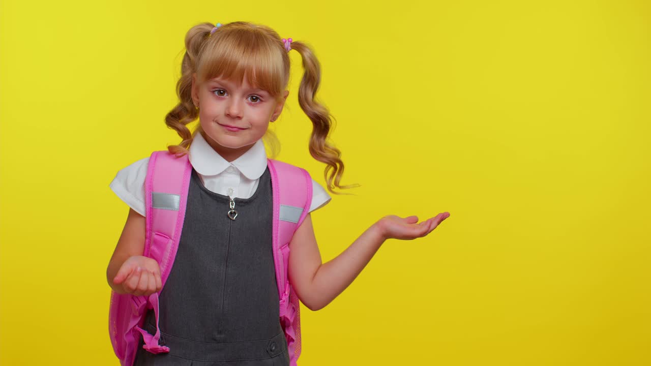 Ein lächelndes süßes Schulmädchen mit Rucksack, das sich einen Platz für Werbeinhalte ansieht und sich die Hand hält
