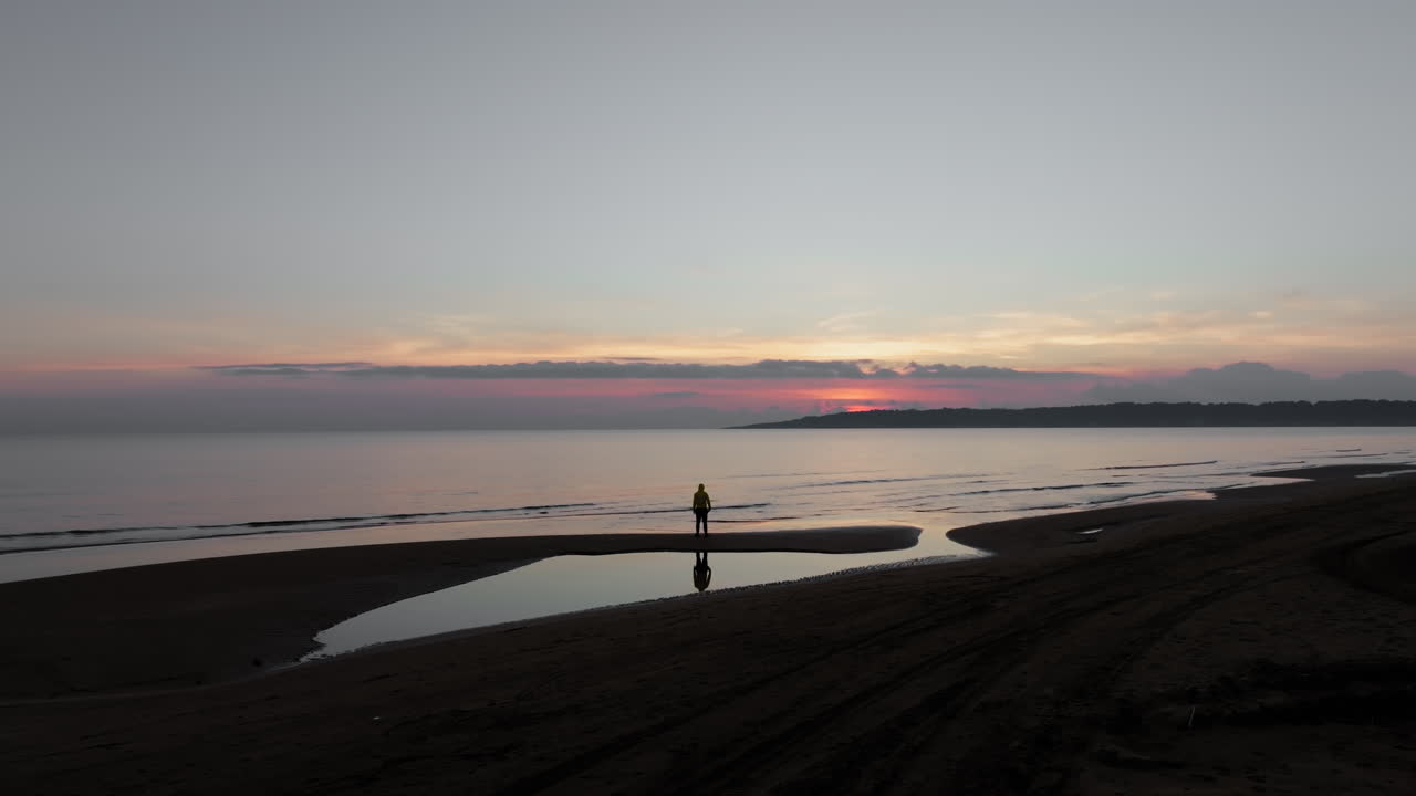 aéreo: fotografía lenta de un avión no tripulado de una persona de pie en la playa de kavouri en grecia durante una tranquila puesta de sol con olas tranquilas