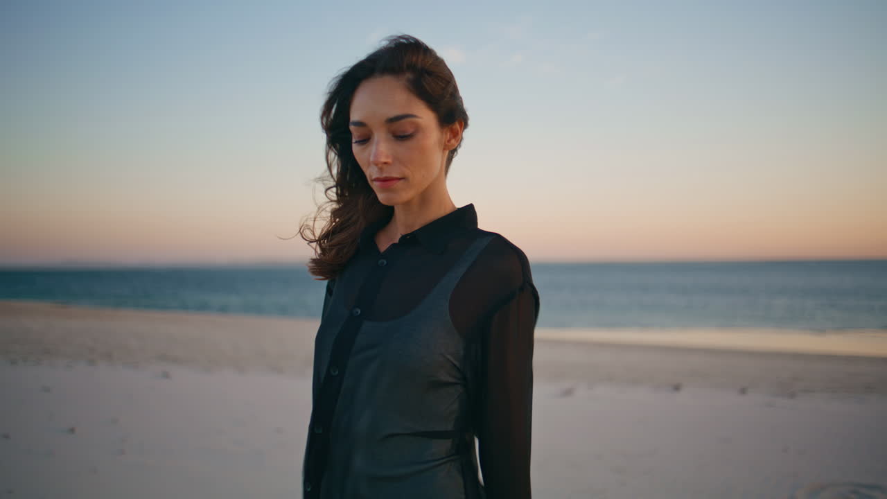 Signora sognante che passeggia sulla costa al mattino presto. Mora tranquilla che cammina sulla spiaggia all'alba
