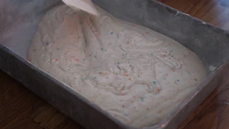 spreading out and evening white funfetti cake batter or frosting with rainbow sprinkles using a rubber spatula and spinning the pan, in 4k 60fps