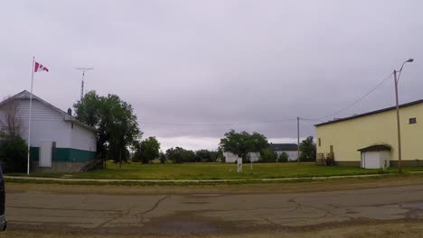 View-of-a-couple-buildings,-a-yard,-and-a-Canadian-flag-in-a-small-town-on-a-cloudy-day