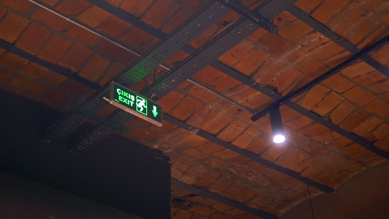 una señal de salida verde colgando de un techo de ladrillo