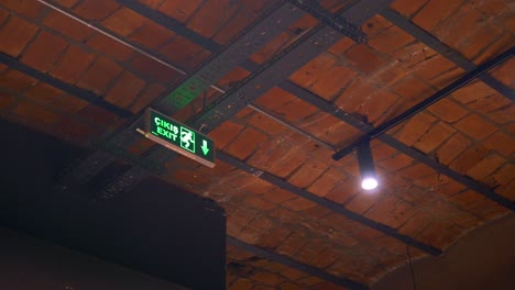 una señal de salida verde colgando de un techo de ladrillo