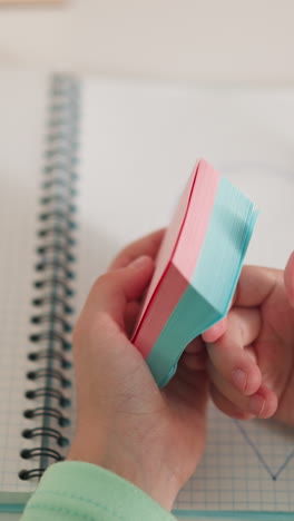 pequeña estudiante de escuela da vueltas coloridas notas de nota sobre el cuaderno sentado en el escritorio de primer plano. alumna juega con pegatinas de nota en la mesa en el aula