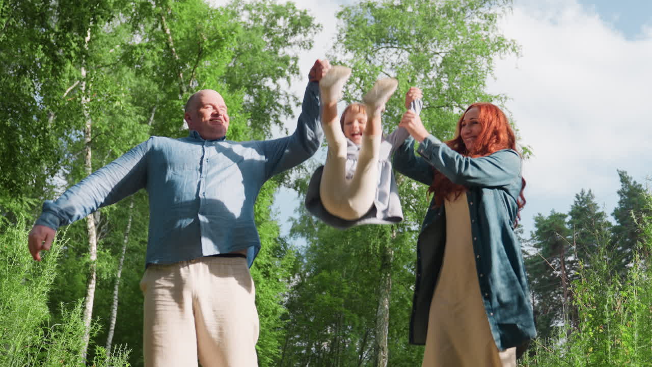 Happy parents walking with daughter on forest path, holding hands and joyfully lifting her between them, surrounded by green trees, expressing love, and togetherness during peaceful family stroll