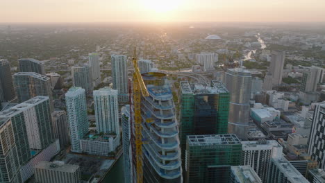 Orbit-shot-around-crane-and-top-of-construction-of-skyscraper.-Aerial-view-of-group-of-high-rise-downtown-buildings.-Miami,-USA