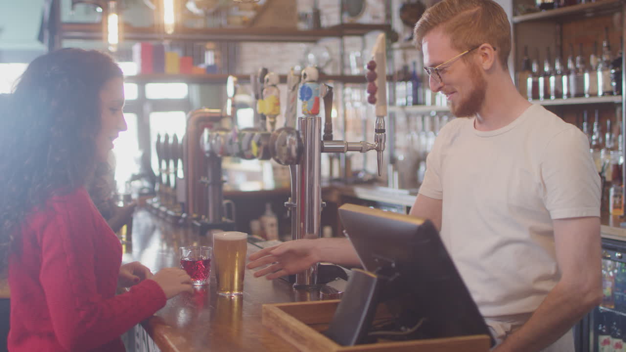 una cliente femenina en un bar hace un pago sin contacto socialmente distante por las bebidas en una pandemia de salud