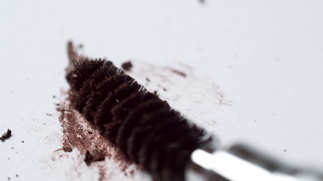 Blending a dark-brown toned mascara loose powder using an eyelash wand applicator on a blank white board