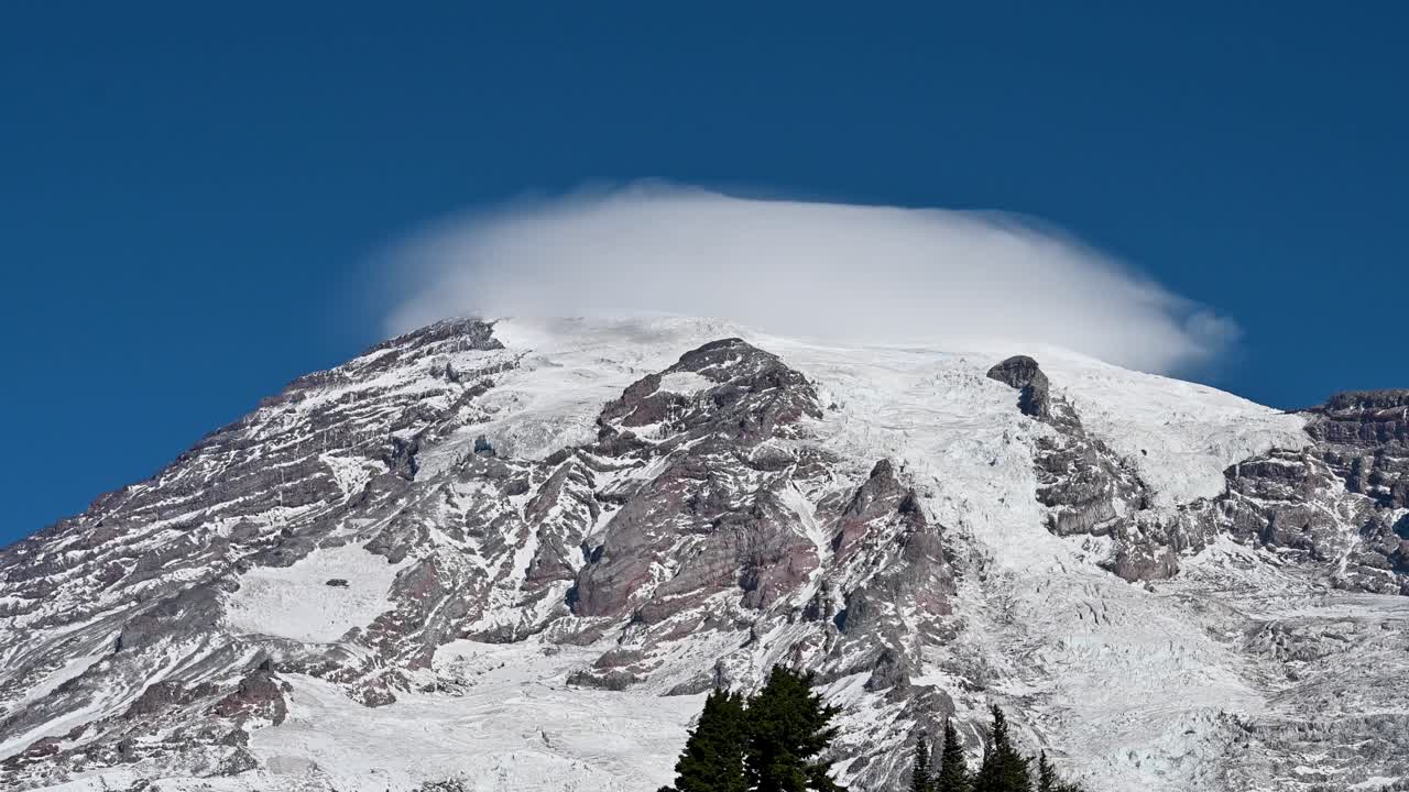 Aerial drone shot of snow-covered mountain peak with lenticular cloud formation above summit