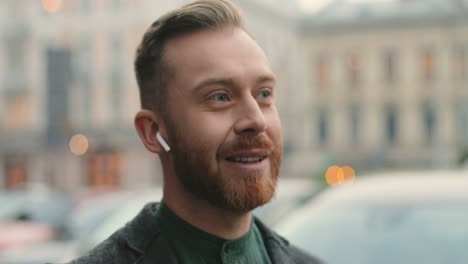 close-up beeld van een blanke zakenman met een baard die draadloze koptelefoons draagt terwijl hij in de herfst op straat telefoneert