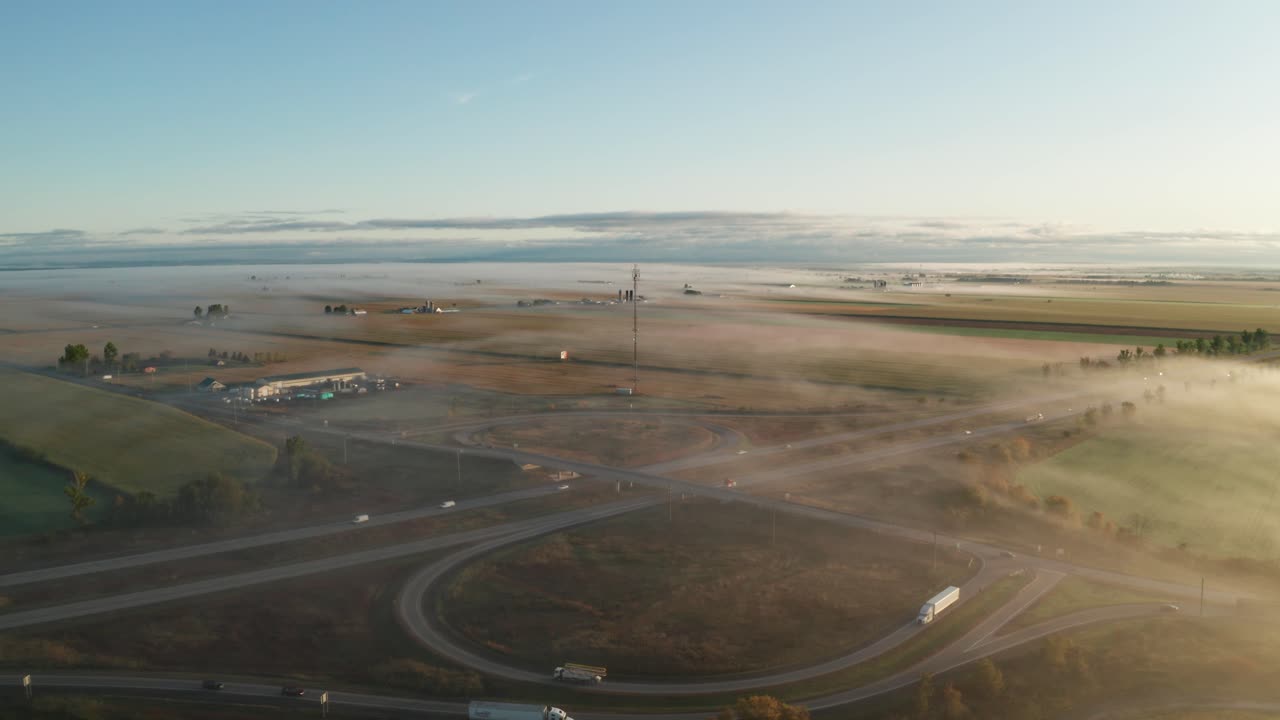 Ascending aerial view of highway interchange in morning light with layer of fog over road and landscape. Driving conditions and road hazard. Commercial trucking and transportation concept.
