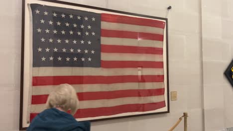 Looking-at-an-old-framed-American-flag-hanging-on-the-wall-of-the-Utah-State-capital-building,-and-a-blonde-woman-walks-by