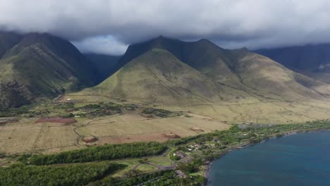 Lush-Maui-landscape-with-towering-green-mountains-and-a-vibrant-coral-reef-coastline,-aerial-view