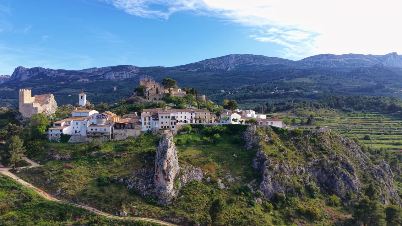 Guadalest historiske bjerglandsby og middelalderborg beliggende på en klippefremspring i Alicante, Spanien, omgivet af grønne dale og bjerglandskab.