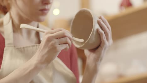 hands of female potter scraping wet clay bowl with wooden tool