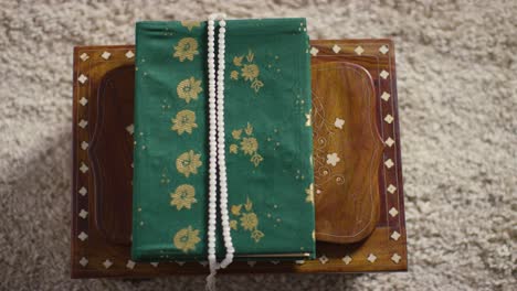 close up of closed copy of the quran on stand at home with prayer beads