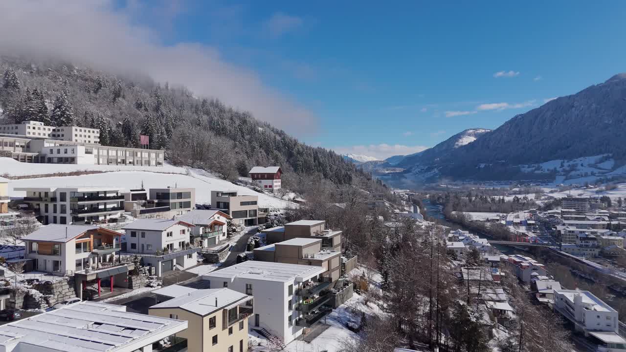 Upper class houses and homes on snowy hill in Swiss Town. Beautiful mountain view during sunny day. Aerial orbit wide shot. Establishing scene. Tranquil and quaint atmosphere on cold clear day.
