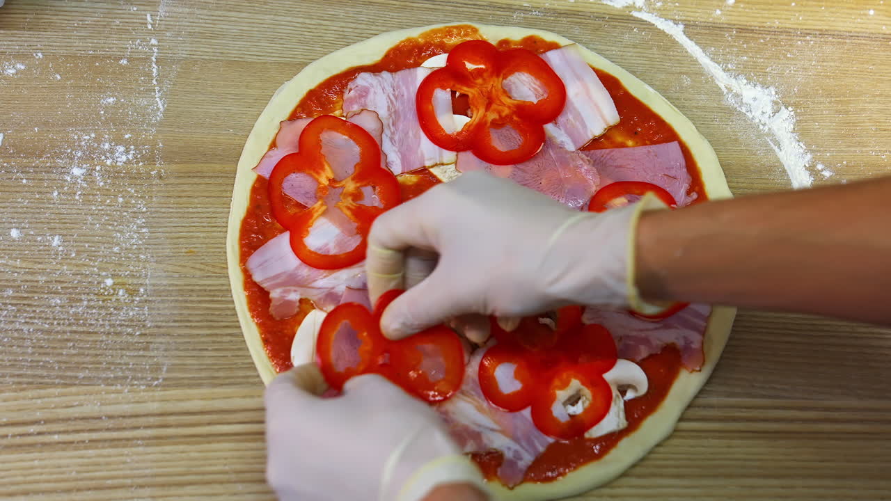 Making pizza in a restaurant. Cooking of pizza. Chef's hands spread pieces of tomatoes on pizza. Top view.