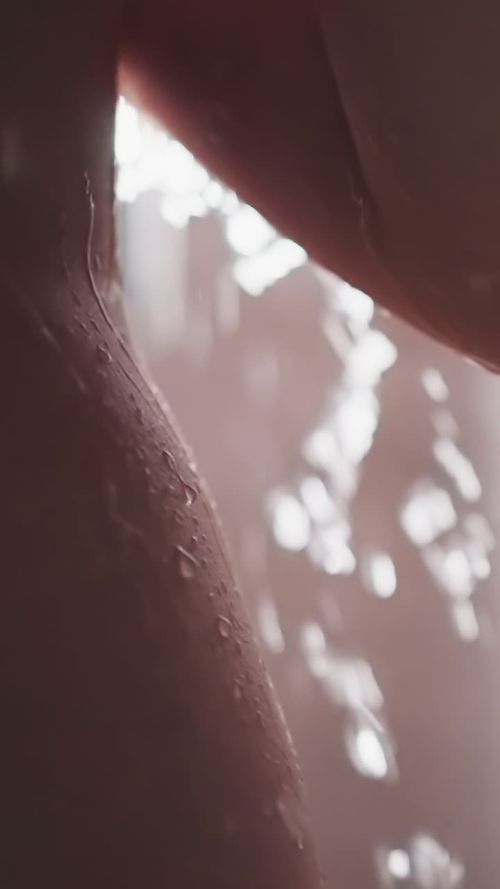 Lady stands in shower with droplets flowing down body. Bare woman takes shower washing body with help of warm water. Cleansing procedure in light shower