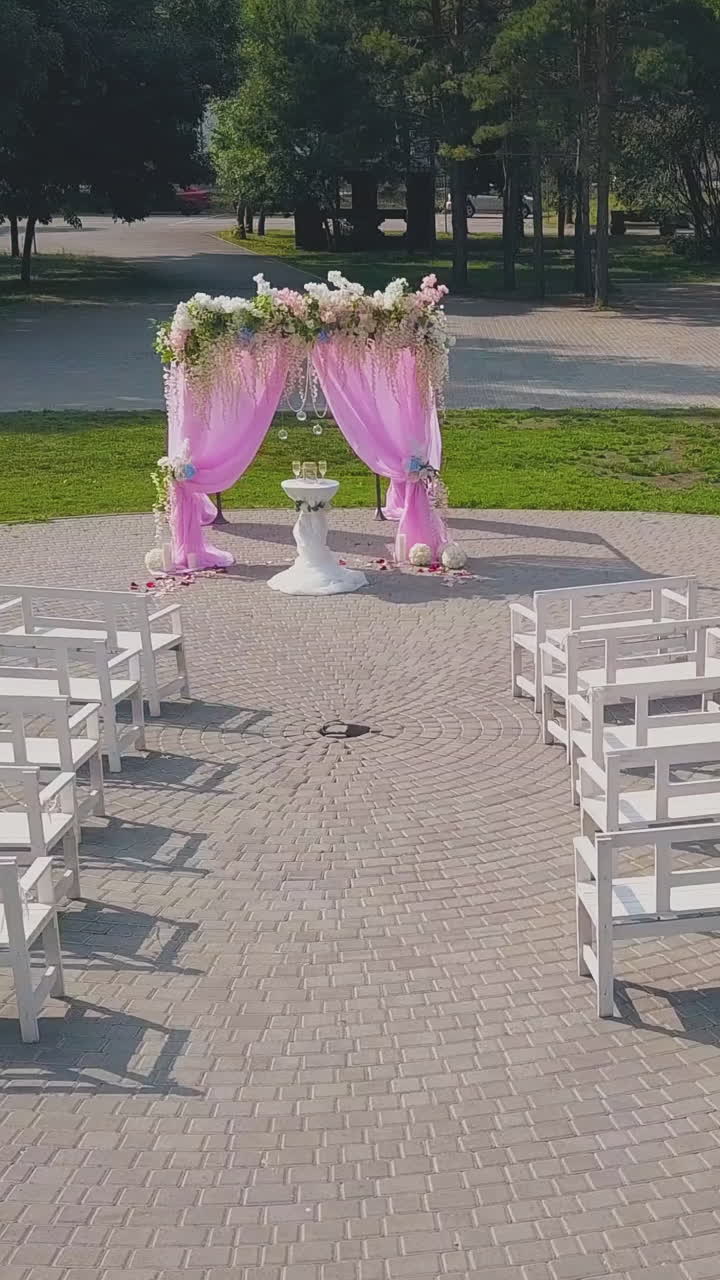 elegant wedding ceremony site decorated with pink chiffon and flowers and guest benches in green park upper view